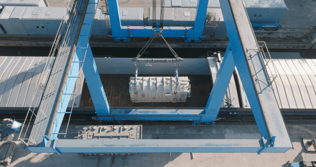 Mit einem Riesenkran wird der Transformator vom Schiff auf den Zug gehoben.