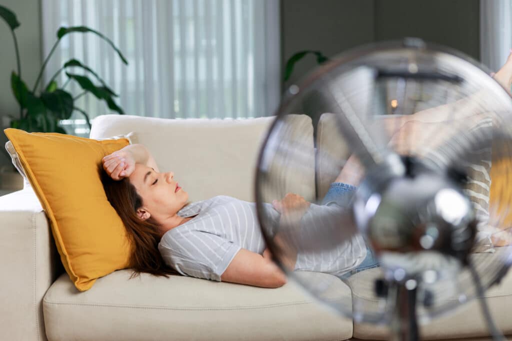 Woman resting in front of electric fan during heatwave Frau liegt am Sofa und im Vordergrund läuft ein Ventilator