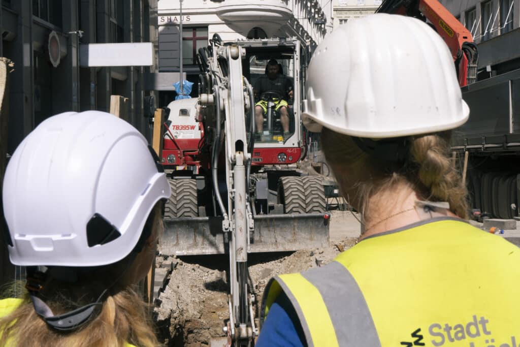 Fernkaelte7 2 Frauen mit Helm von hinten vor einem Bagger